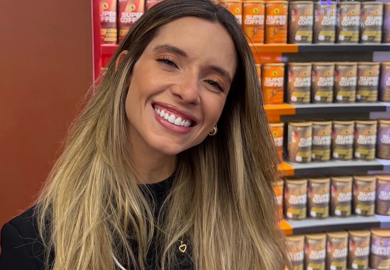 Sthéfany sorrindo em frente a uma prateleira de produtos, na feira Natural Tech