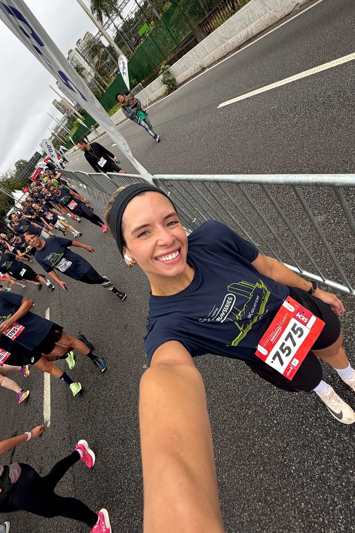 Selfie de Sthéfany sorrindo no meio de corredores, com camisa azul-marinho e número de prova vermelho